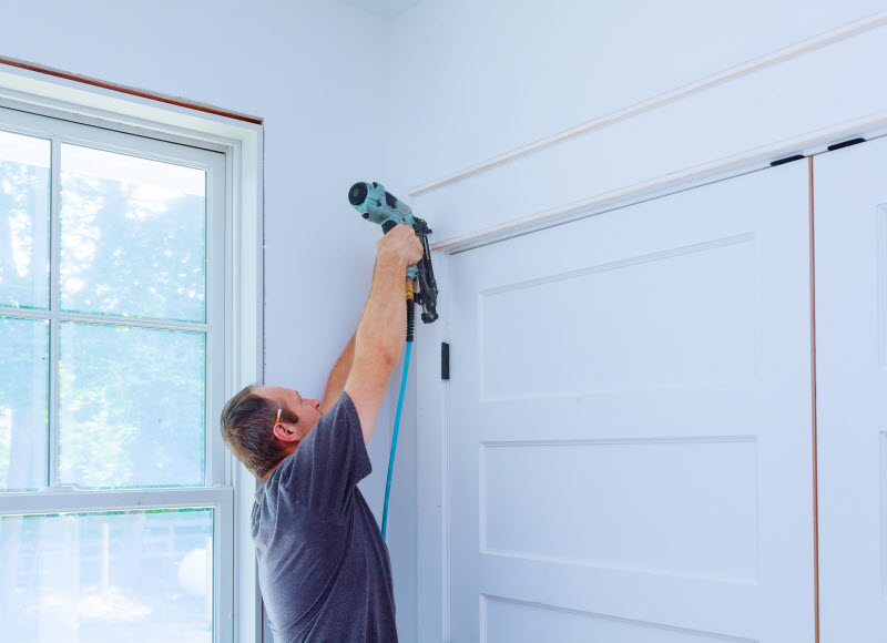 Carpenter using nail gun to moldings on doors at home